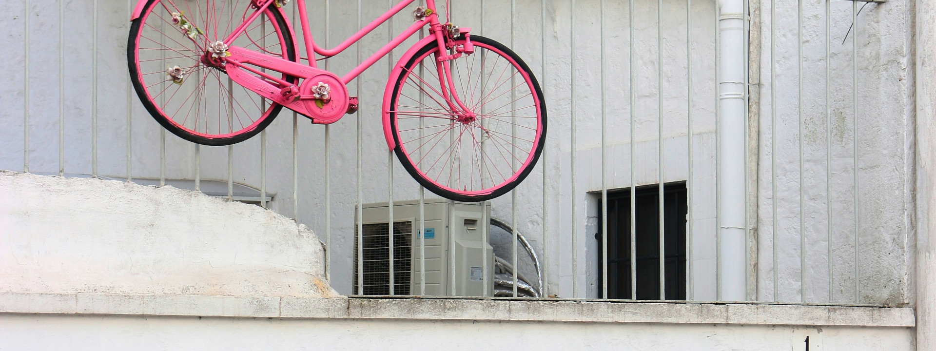 Ein knallpinkes Fahrrad, dass über ein Gitter eines Gebäudes hängt.