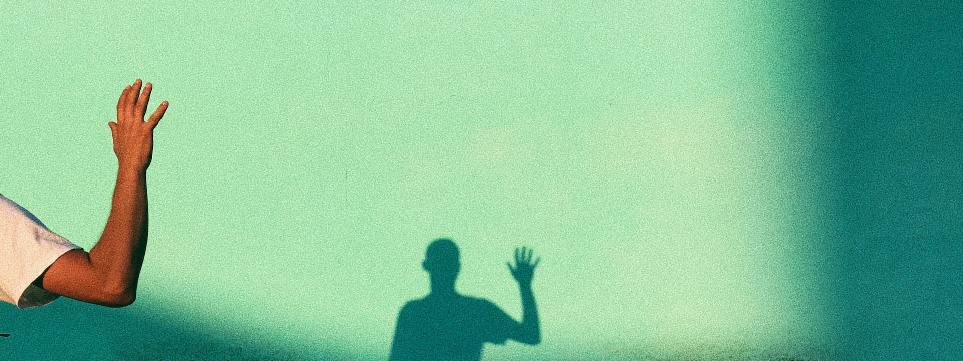 Eine gehobene Hand wirft einen Schatten auf eine grüne Wand.